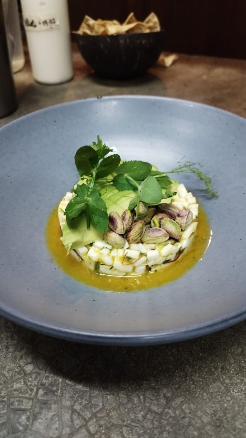 Ceviche de coco con aguacate, pistache y brotes en plato azul grisáceo