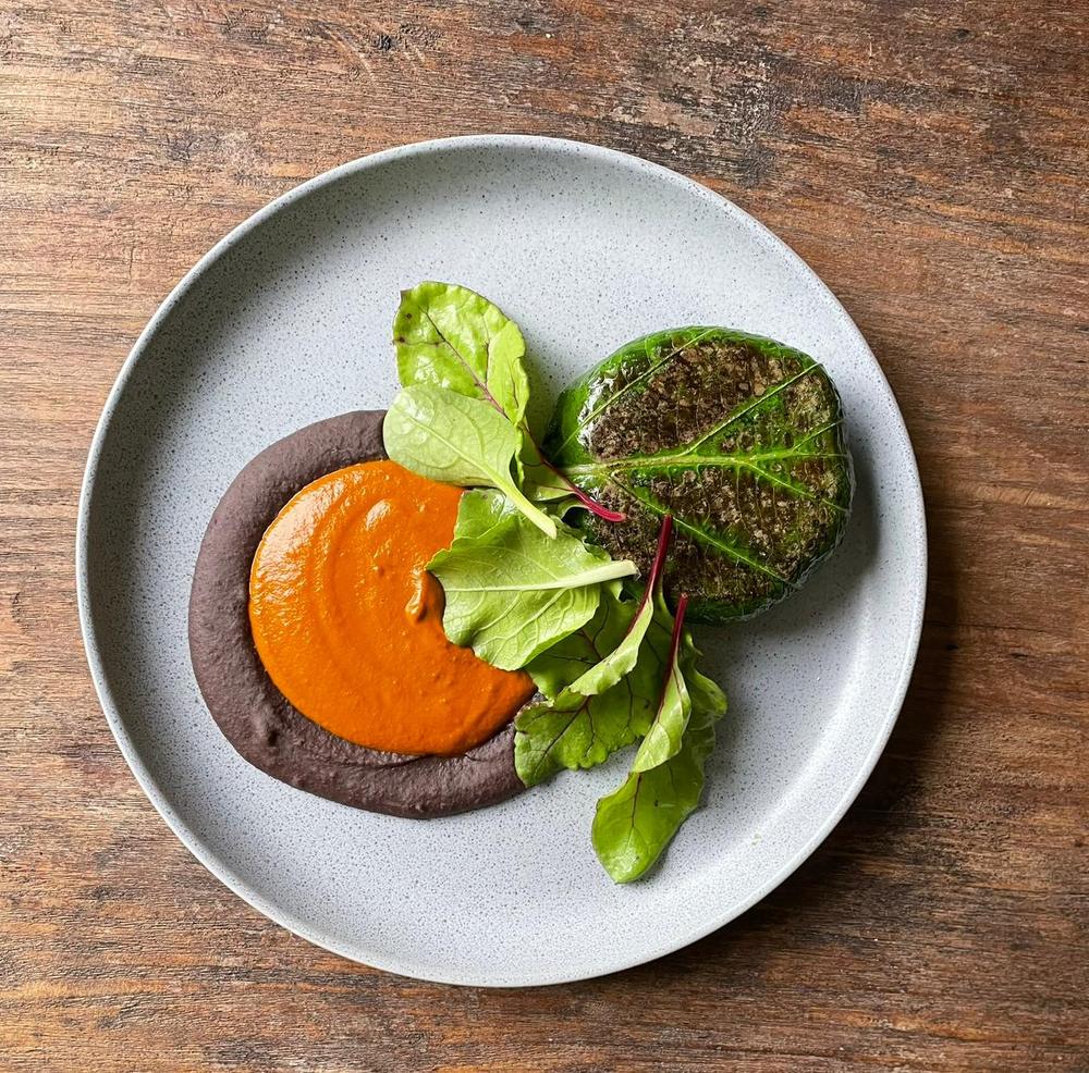 Gordita de plátano en hoja santa sobre pipián rojo y frijol, con hojas verdes
