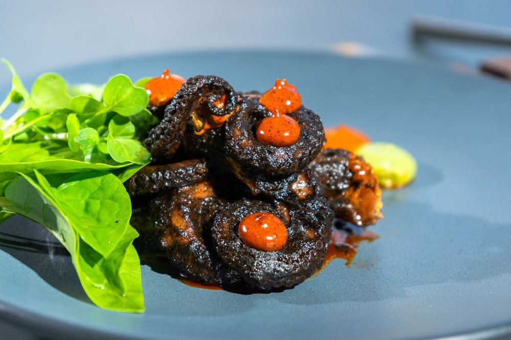 Pulpo a la talla en trozos con salsa roja y hojas verdes