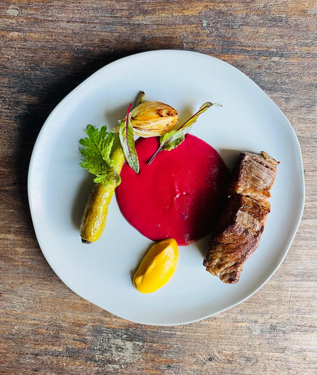 Rib eye rebanado junto a un mole rosa, con camote y zanahorias glaseadas
