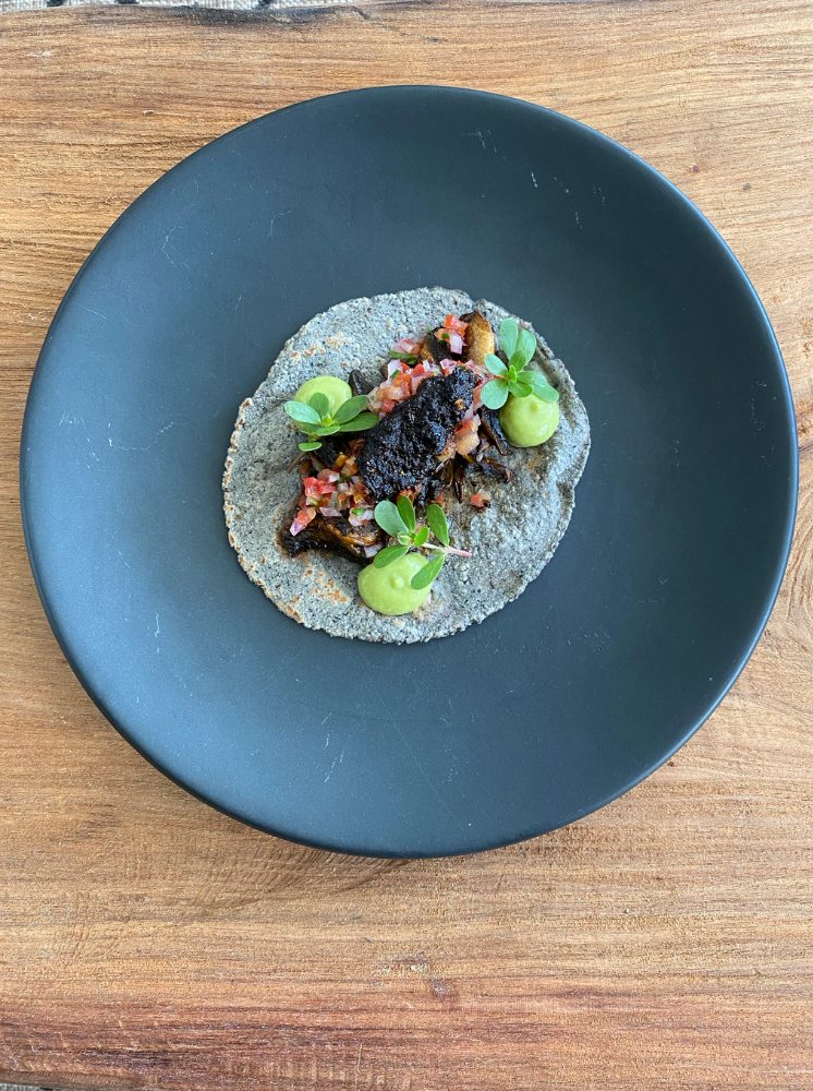 Taco de hongos salteados con salsa macha sobre tortilla azul en plato oscuro